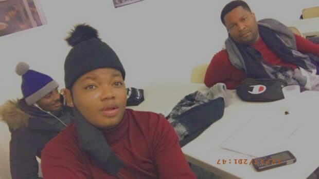 Three people sitting indoors, wearing winter clothing and looking toward the camera.