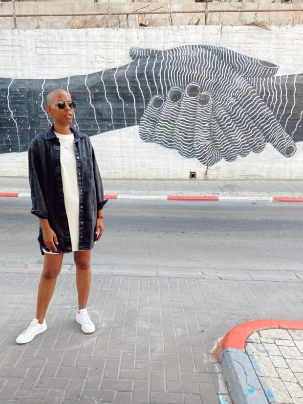 Person standing on a sidewalk in front of a mural depicting two hands shaking.