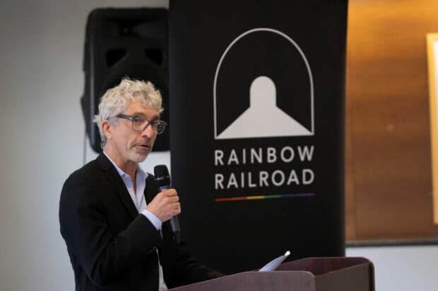 A person speaks at a podium with a Rainbow Railroad banner behind them.