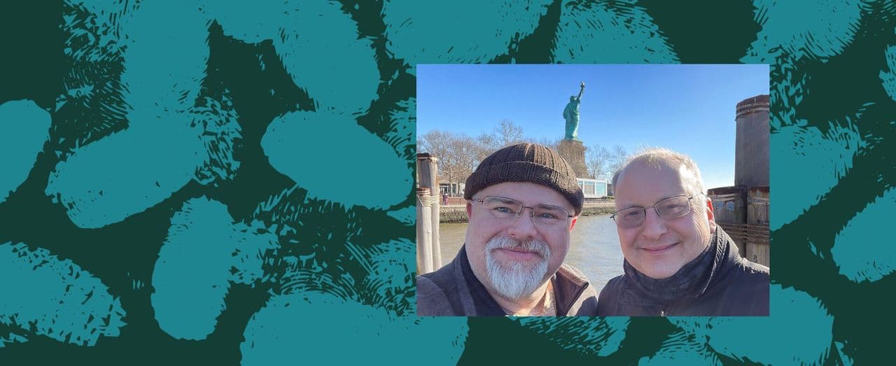 Two people smiling together outdoors with the Statue of Liberty in the background.