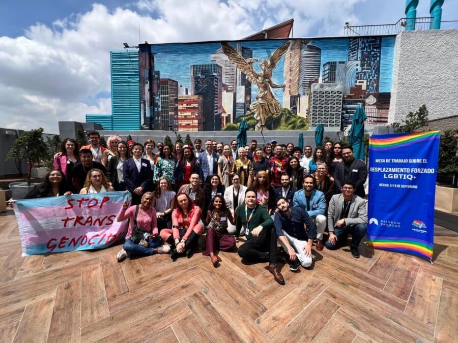 Large group of people posing outdoors, holding banners supporting LGBTQ+ and trans rights.