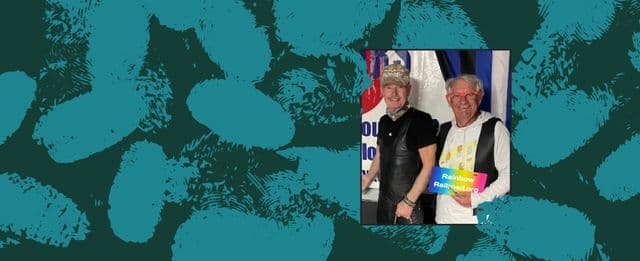Two people smiling together at an event holding a Rainbow Railroad sign, with a patterned teal background.