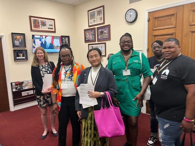 Group of people standing in an office holding papers during a meeting.
