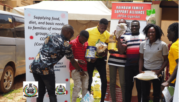 Group of people distributing food and supplies outdoors beside Rainbow Family Support Alliance (RFSA-Uganda) banners.