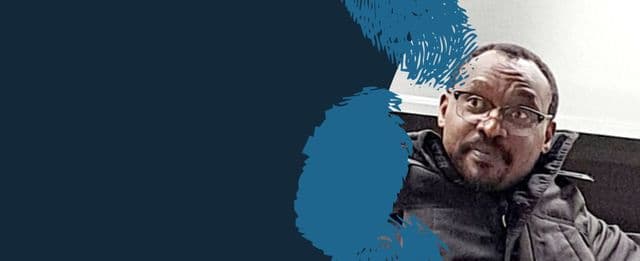 Person wearing glasses and a dark jacket against a navy blue background.