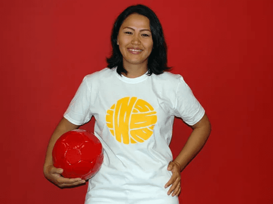 Person smiling and holding a red soccer ball while standing against a red wall.