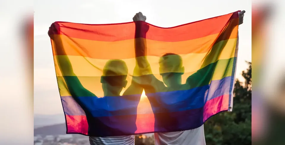 Two people holding a pride flag behind them