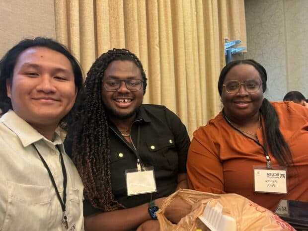 Three people smiling and seated at a conference table.