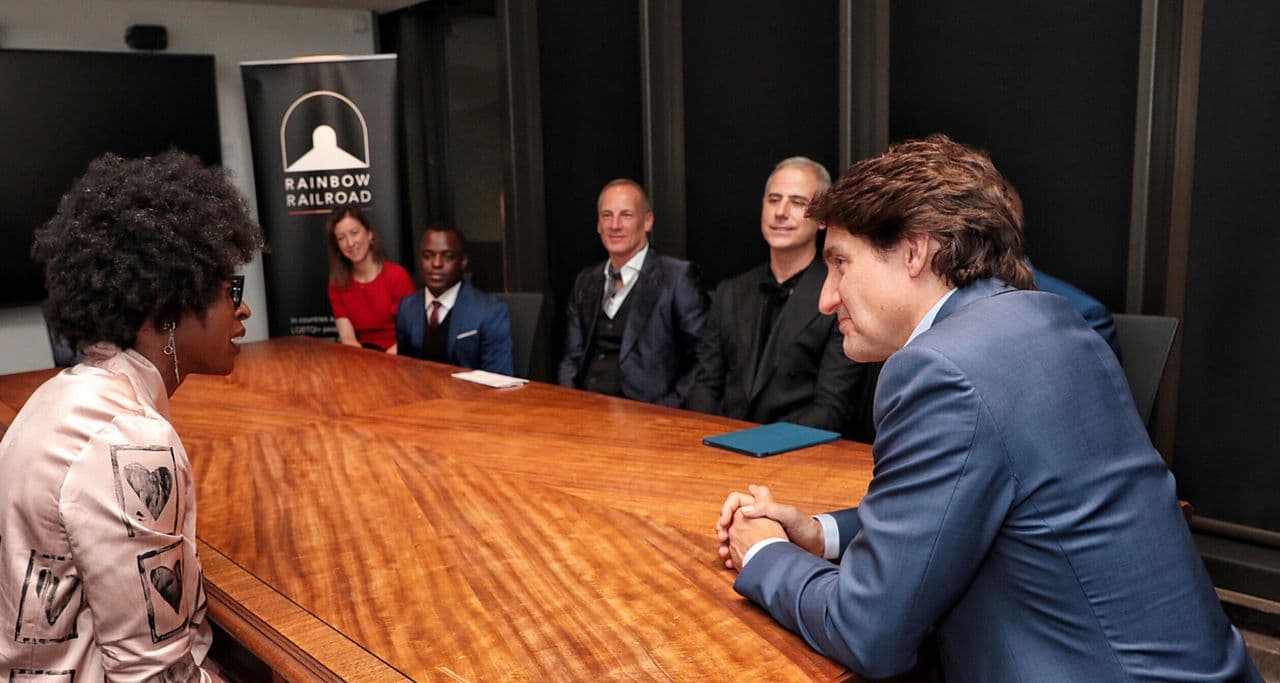 People seated around a conference table in discussion, with a Rainbow Railroad banner visible in the background.